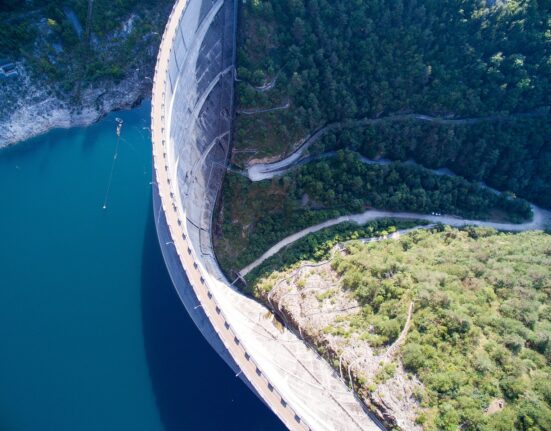 Aerial view of a large dam surrounded by water and forest.